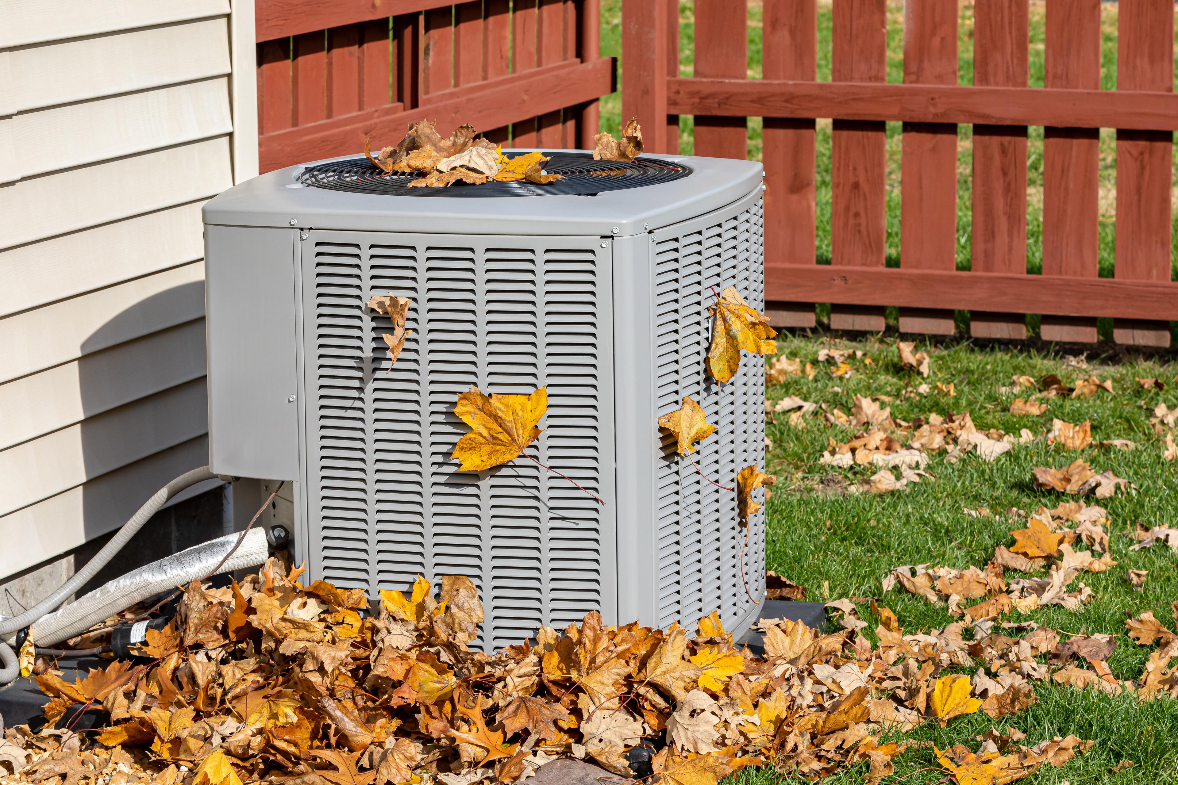 An outdoor HVAC unit surrounded by fallen autumn leaves